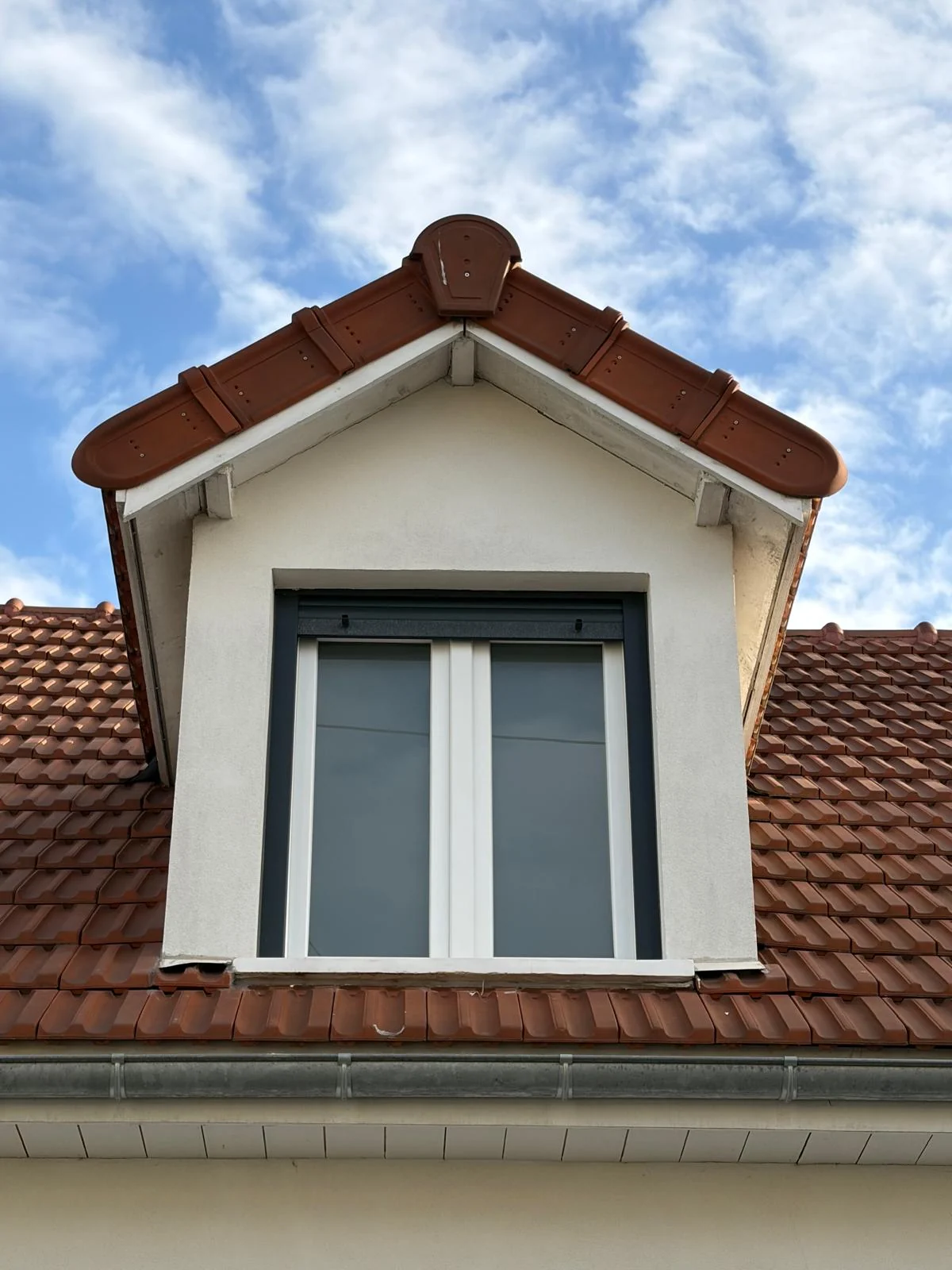 Lucarne blanche sur une couverture en tuiles rouges.