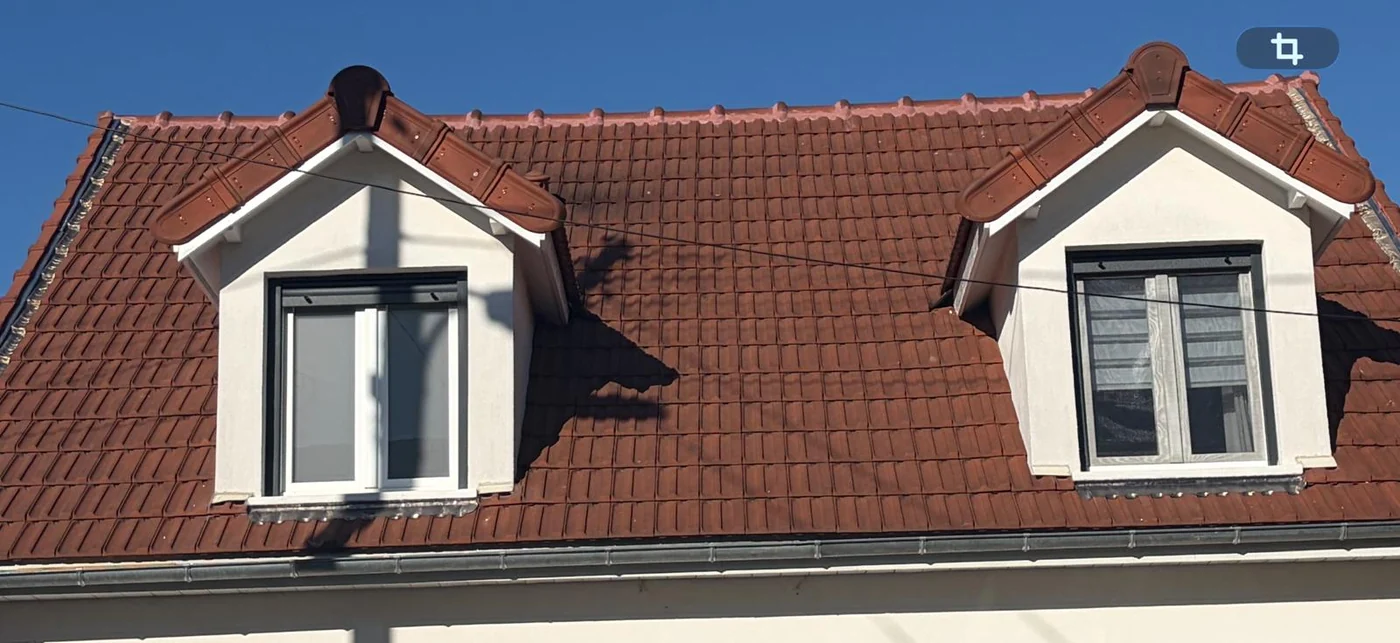 Deux lucarnes blanches sur une couverture en tuiles.